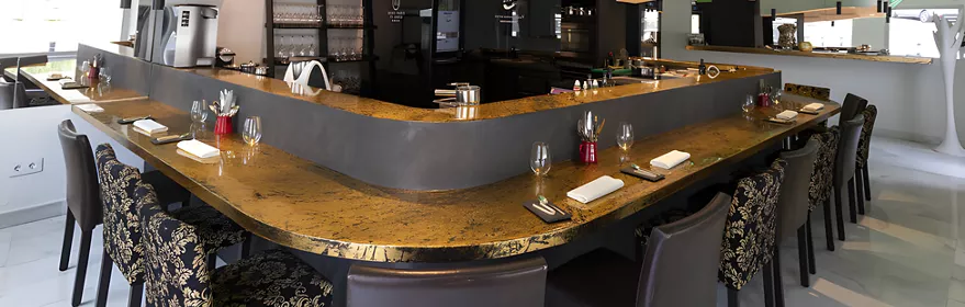 Cocina abierta con barra central, techo verde iluminado y mesas altas