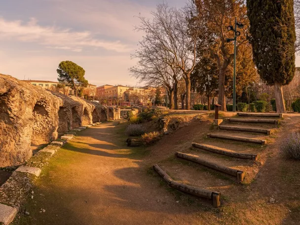 Paseo junto a ruinas de piedra con escalinata de madera y árboles al atardecer.