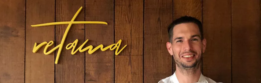 Chef posando ante pared de madera con logotipo Retama