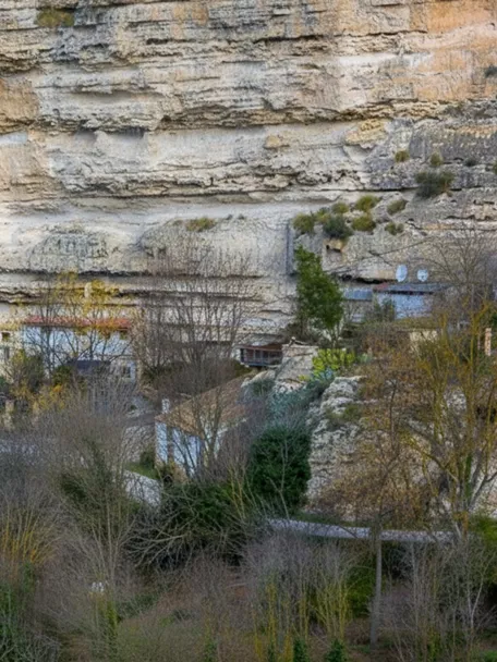 Casas junto a un río de agua turquesa, bajo una pared rocosa estratificada.