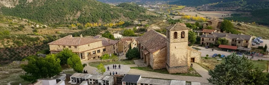 Vista aérea de conjunto rural con iglesia y montañas al fondo.