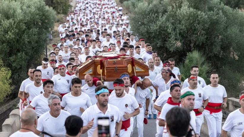 Multitud numerosa corriendo en fila por una carretera arbolada mientras llevan un féretro.