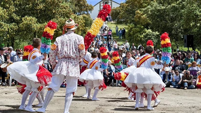Grupo de danzantes con trajes tradicionales y adornos de colores ante el público.