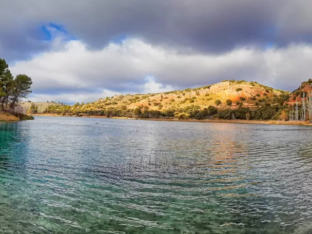 Laguna de agua clara rodeada de vegetación y colinas.