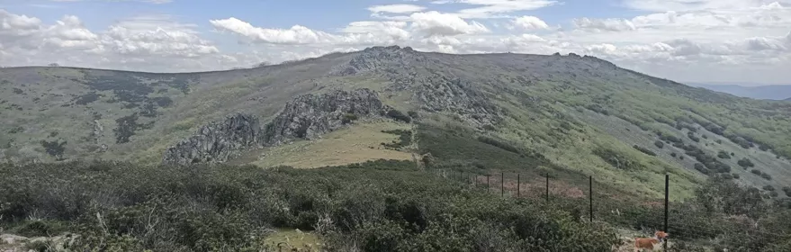 Vista de cresta montañosa con matorral y cielo parcialmente nublado.