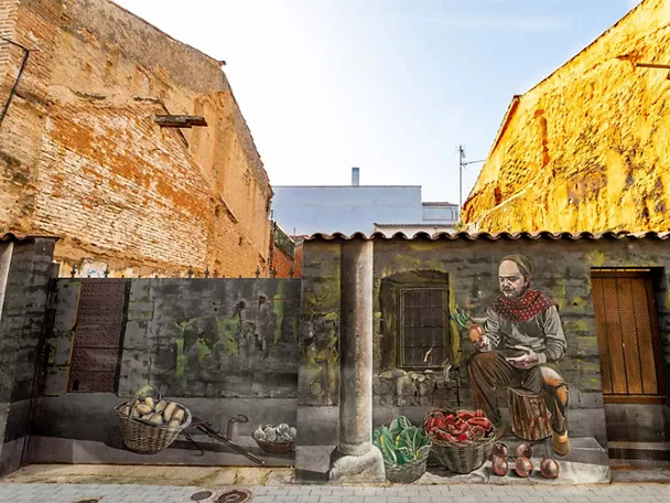Mural de hombre sentado frente a una casa antigua con cestas de verduras.