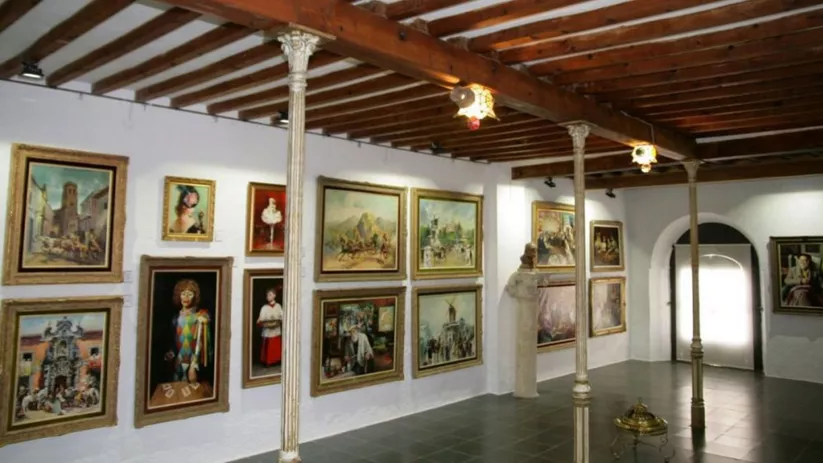 Sala expositiva con pinturas enmarcadas y techo de vigas de madera