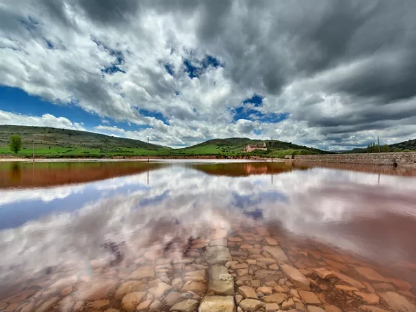Lámina de agua rojiza bajo cielo nuboso