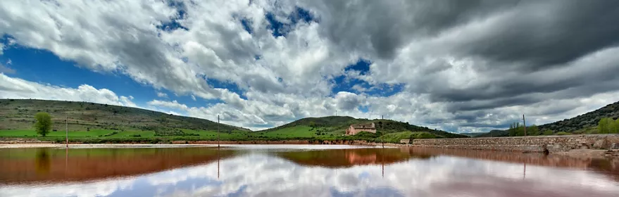 Edificio de piedra junto a estanques de sal y campos amarillos.