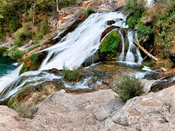 Cascada natural que cae sobre rocas cubiertas de musgo hacia una poza de agua turquesa.
