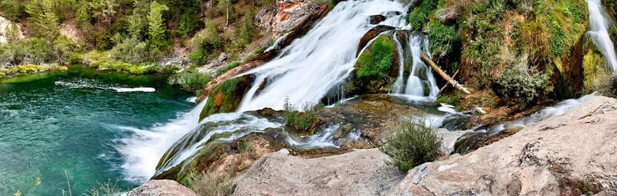Cascada natural que cae sobre rocas cubiertas de musgo hacia una poza de agua turquesa.
