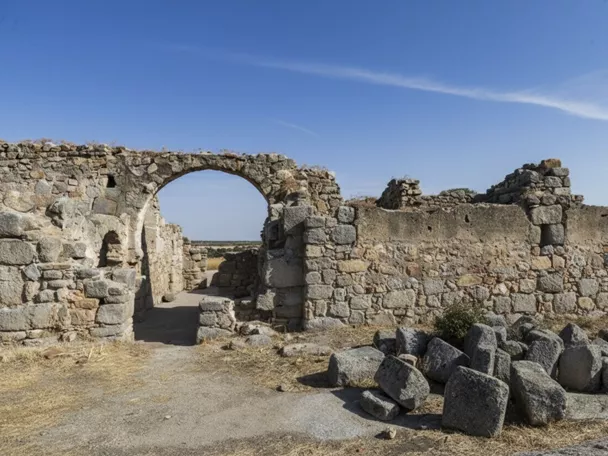 Muros de piedra en ruinas con arco y rocas en primer plano.