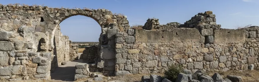 Muros de piedra en ruinas con arco y rocas en primer plano.