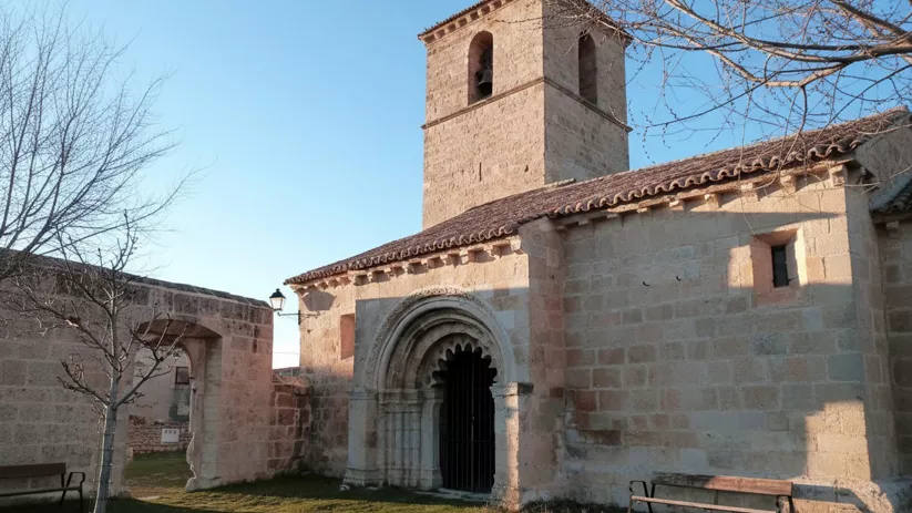 Iglesia de piedra con torre cuadrada y banco exterior.