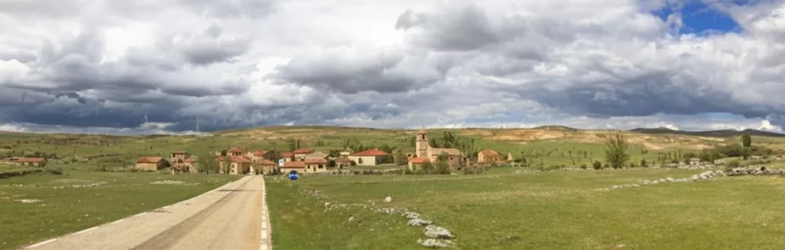 Carretera hacia pequeño pueblo entre campos verdes.