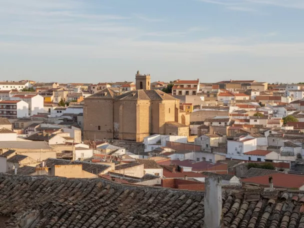 Una vista de la torre de una iglesia y tejados de casas desde una calle estrecha, bajo un cielo nublado.