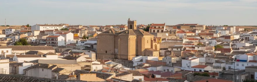 Una vista de la torre de una iglesia y tejados de casas desde una calle estrecha, bajo un cielo nublado.