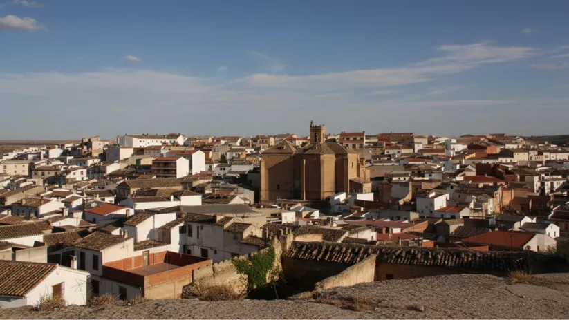 Una vista de un pueblo desde un terreno rocoso, con una iglesia de piedra en el centro y casas de tejados rojos.