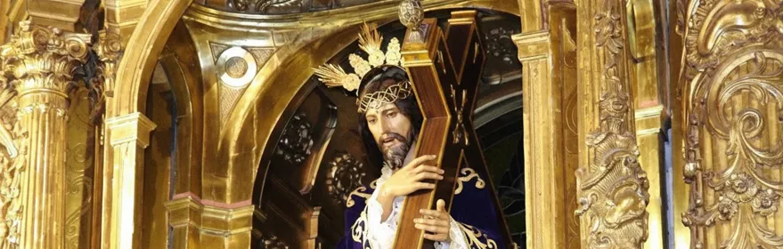 Escultura religiosa con cruz en retablo dorado y flores blancas.