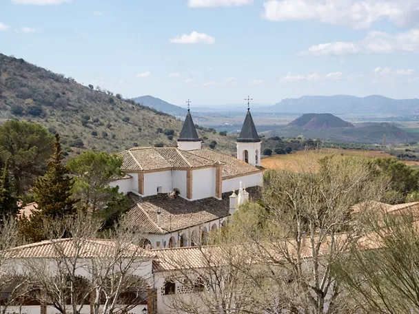 Edificio religioso blanco con dos torres, rodeado de colinas y campos.