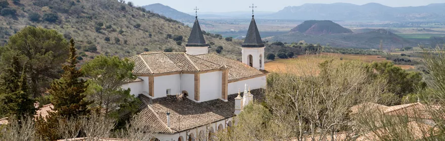 Edificio religioso blanco con dos torres, rodeado de colinas y campos.