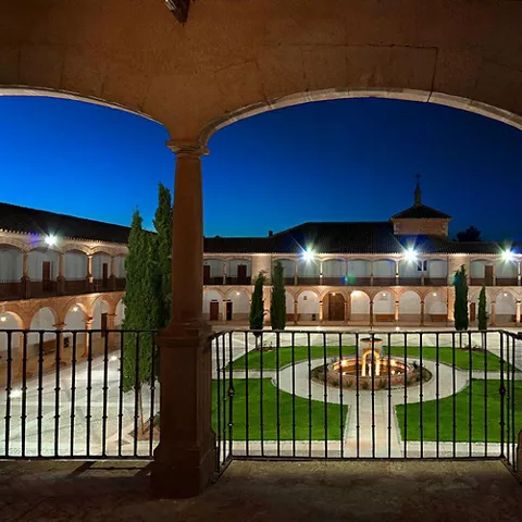 Claustro iluminado con arcos y jardín central al anochecer