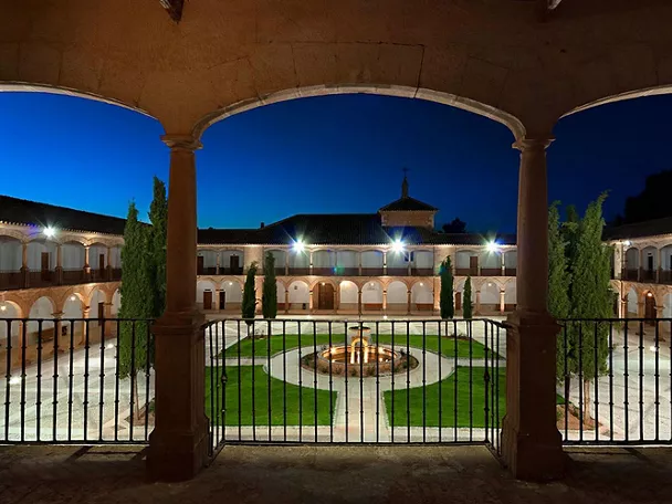 Claustro iluminado con arcos y jardín central al anochecer
