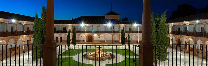 Claustro iluminado con arcos y jardín central al anochecer