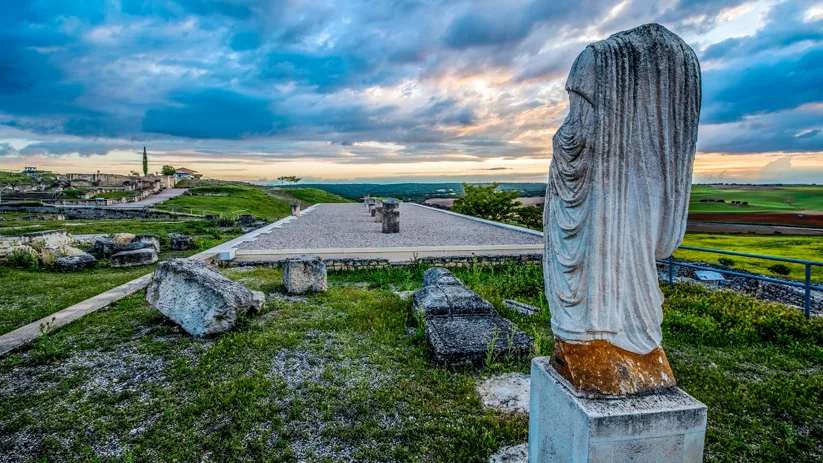 Yacimiento arqueológico medieval con estatua de piedra y paisaje rural.