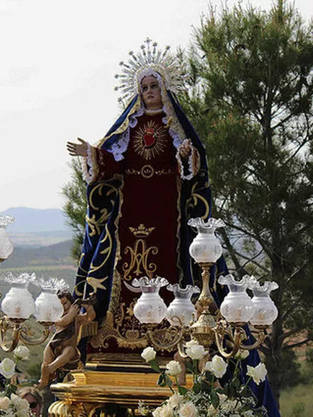 Paso procesional con imagen femenina coronada avanzando por un entorno rural.