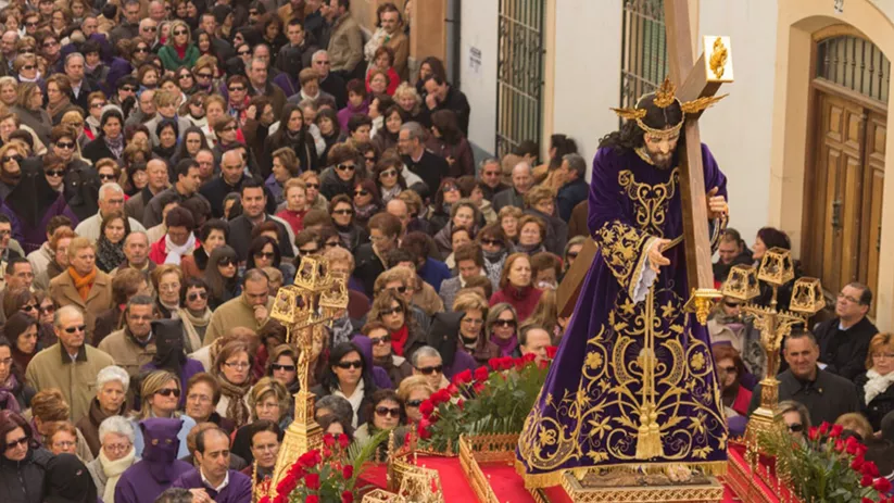 Paso religioso con figura portando cruz entre multitud