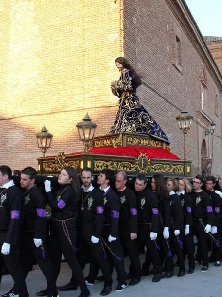Procesión con imagen masculina sobre un paso adornado, llevada por costaleros.