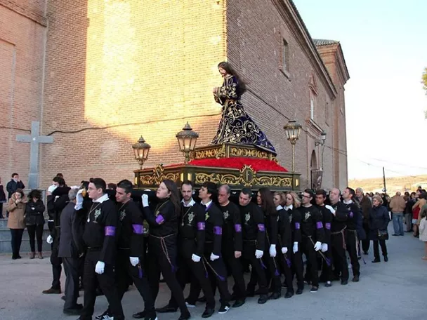 Procesión con imagen masculina sobre un paso adornado, llevada por costaleros.