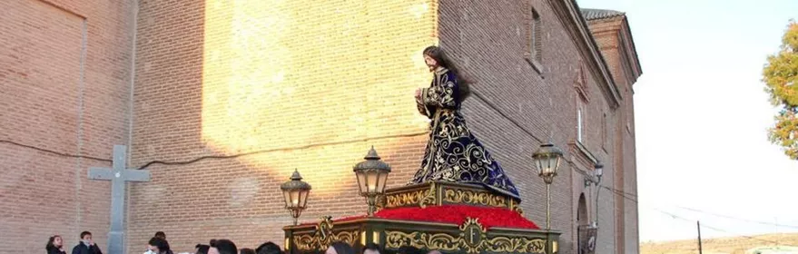 Procesión con imagen masculina sobre un paso adornado, llevada por costaleros.