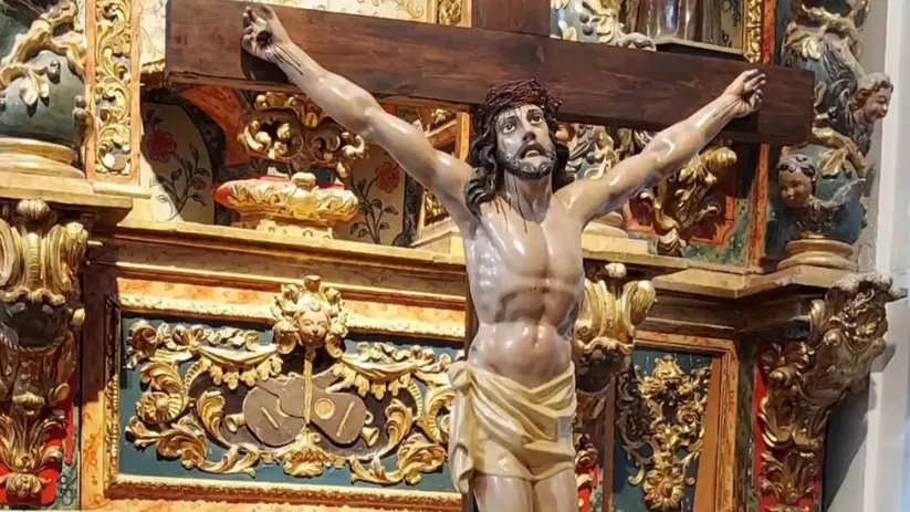 Escultura religiosa de un crucificado sobre un altar decorado con dorados.