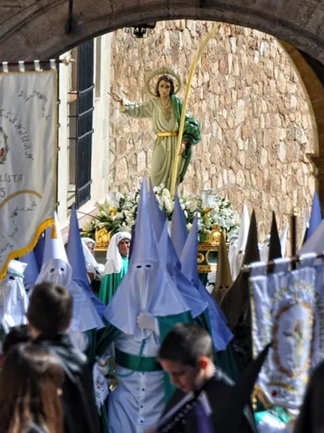 Procesión con personas encapuchadas portando una imagen religiosa bajo un arco de piedra