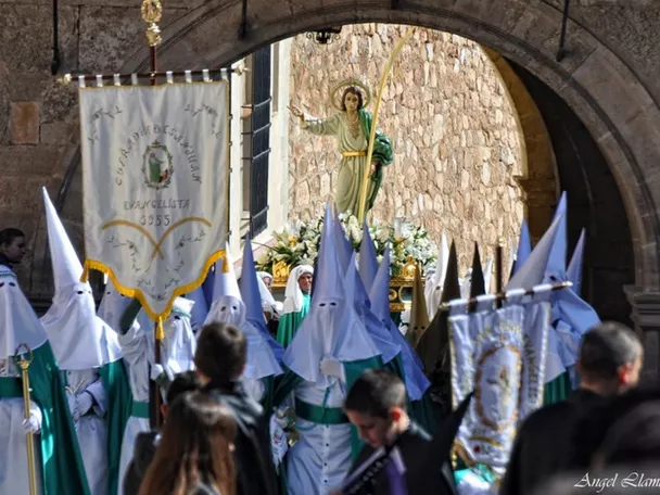 Procesión con personas encapuchadas portando una imagen religiosa bajo un arco de piedra