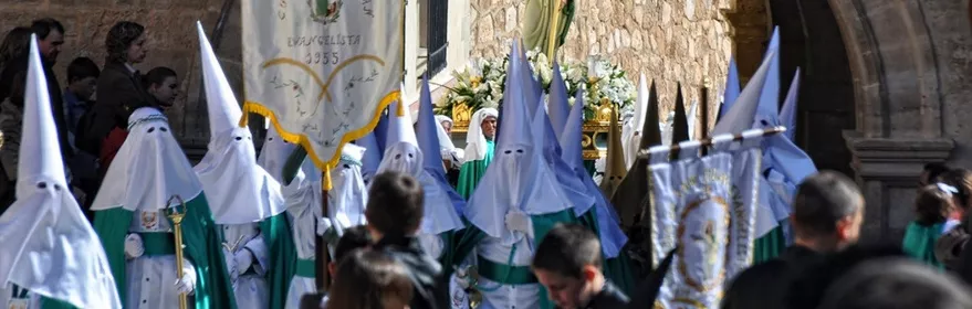 Procesión con personas encapuchadas portando una imagen religiosa bajo un arco de piedra