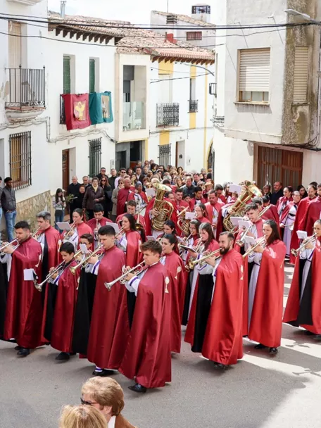 Banda de música desfilando por una calle con túnicas rojas.