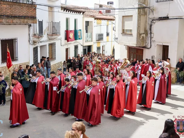 Banda de música desfilando por una calle con túnicas rojas.