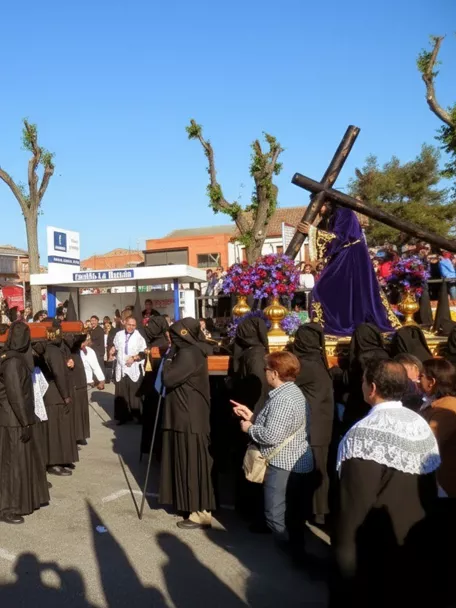 Cofrades vestidos de negro portando andas con imágenes religiosas en plaza concurrida.
