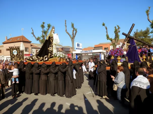 Cofrades vestidos de negro portando andas con imágenes religiosas en plaza concurrida.