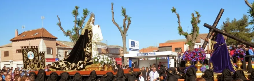 Cofrades vestidos de negro portando andas con imágenes religiosas en plaza concurrida.