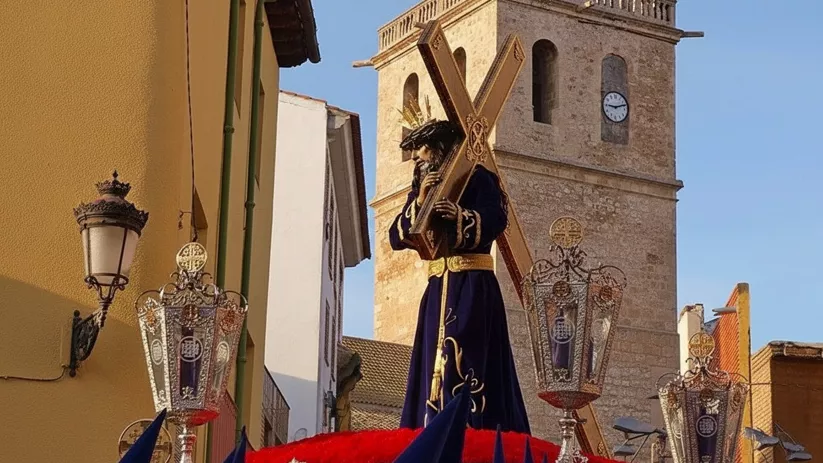 Imagen religiosa con cruz sobre paso adornado con faroles.