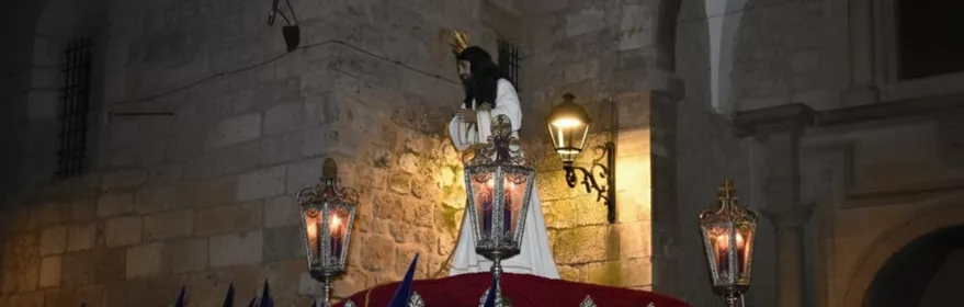 Paso religioso nocturno con nazarenos de túnica azul.