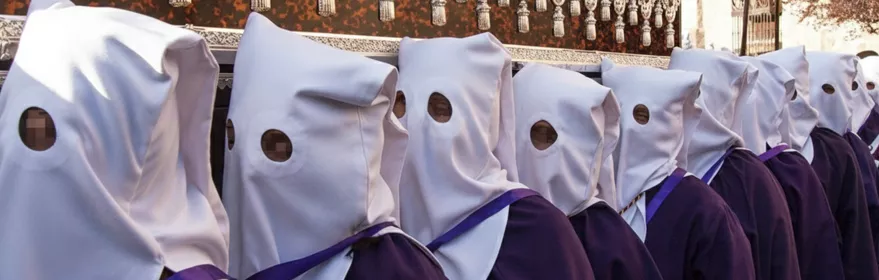 Fila de penitentes con túnicas moradas y capirotes blancos durante una procesión.