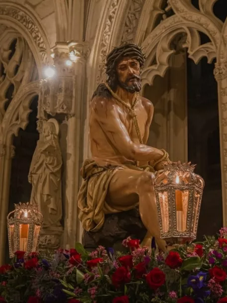 Escultura de Cristo coronado de espinas sobre paso procesional con faroles y flores, en el interior de un templo.