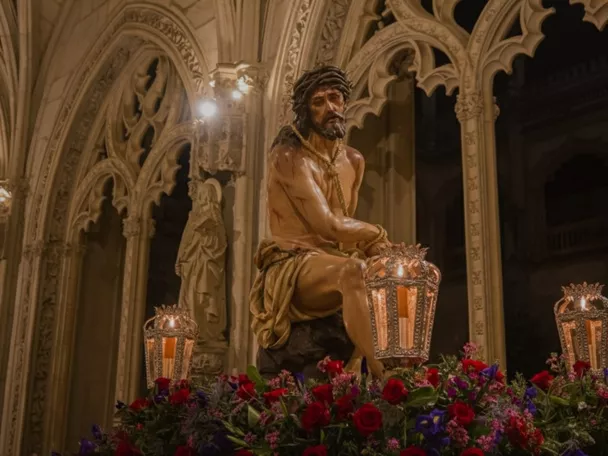 Escultura de Cristo coronado de espinas sobre paso procesional con faroles y flores, en el interior de un templo.