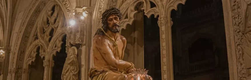 Escultura de Cristo coronado de espinas sobre paso procesional con faroles y flores, en el interior de un templo.