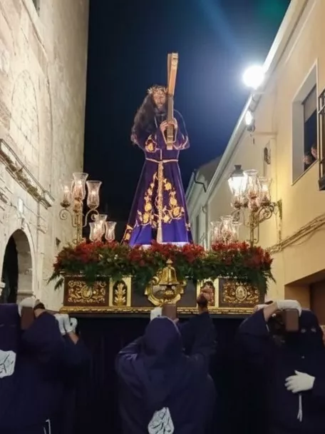 Imagen religiosa sobre andas llevada por cofrades en una calle estrecha de noche.